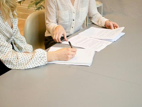 Duas pessoas à mesa com documentos, uma delas assinando